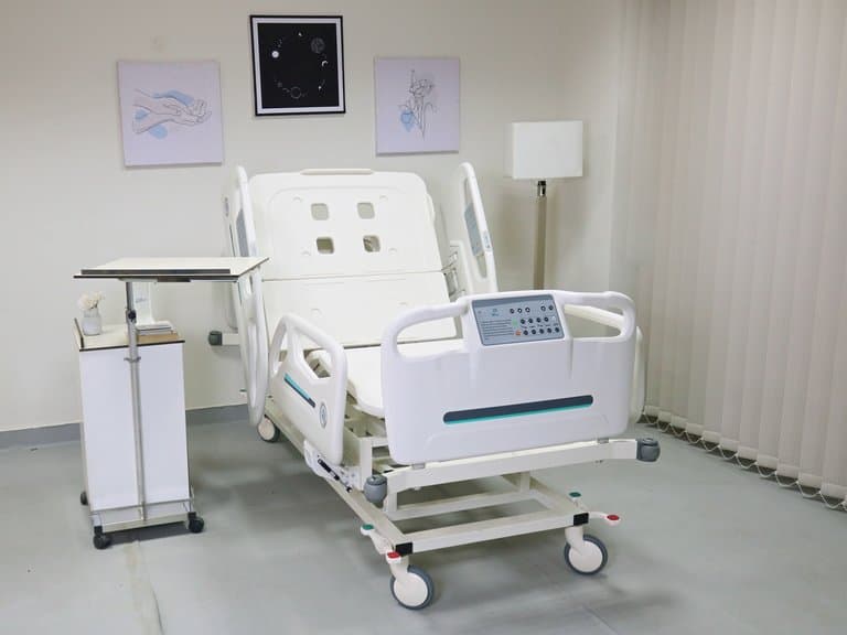 Lit de soins intensifs Santron, dossier relevé, dans une chambre équipée d'une table de lit et d'une table de chevet