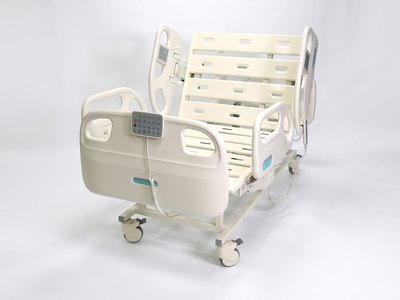 F5 Medical Bed, three-quarter foot-end view, backrest raised, control pad on the foot rail, white studio