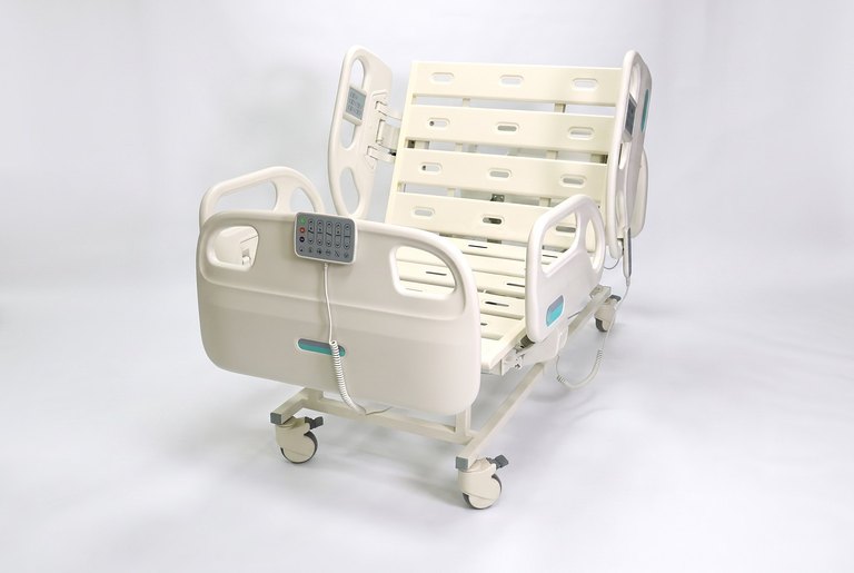 F5 Medical Bed, three-quarter foot-end view, backrest raised, control pad on the foot rail, white studio